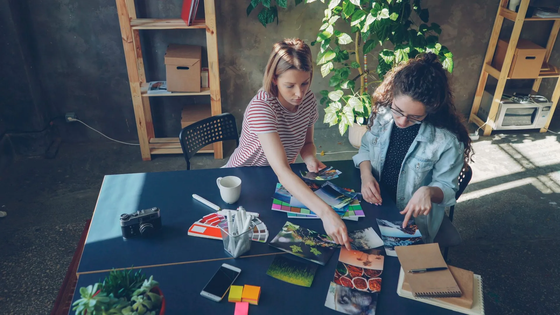 Two women collaborate on a creative project, analyzing photos and color palettes in a modern office.