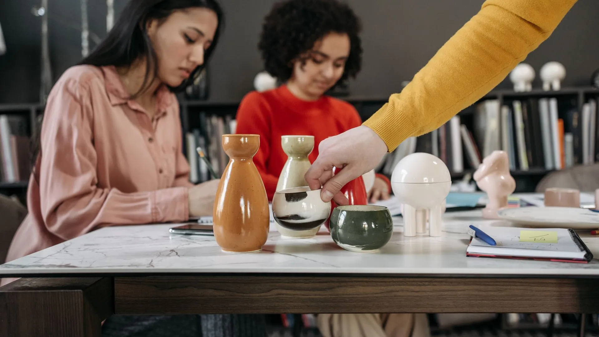 Women collaborating in a stylish office with ceramics and notes on the desk.