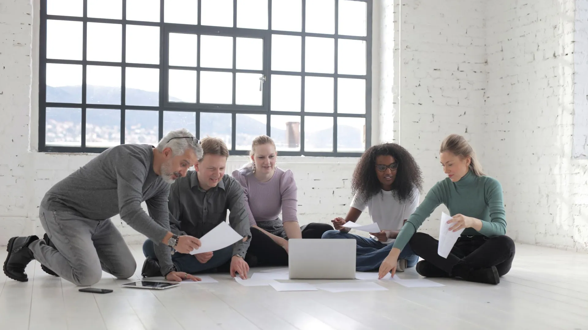 A diverse group of professionals collaborating on a project in a light-filled modern workspace.
