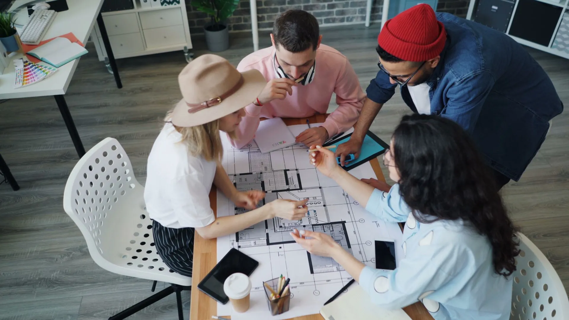 A diverse group of four adults collaborating on architectural blueprints in a modern office setting.